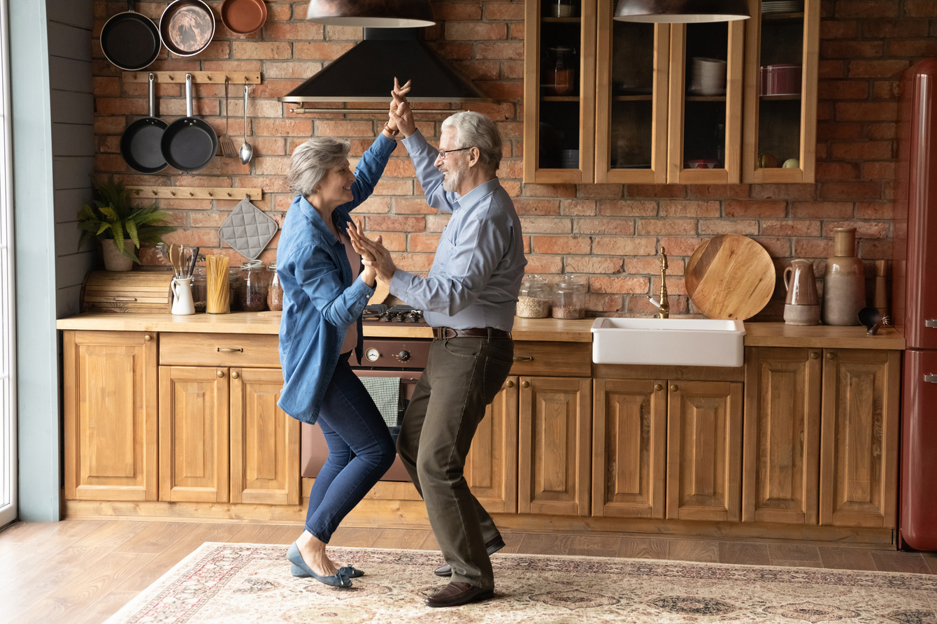 Energetic middle aged family couple dancing in kitchen.